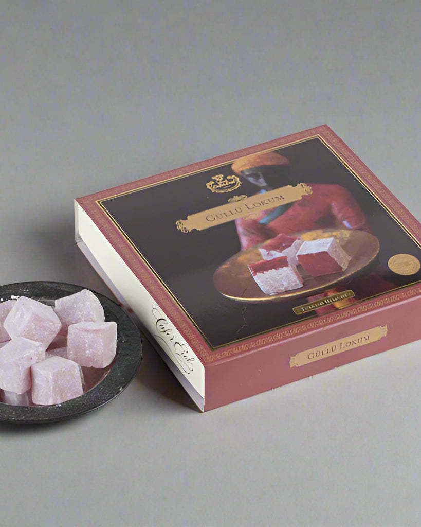 An envelope cardboard box with a floral design, containing rose Turkish delight, displayed on a marble surface with a bowl of the same Turkish delight in front.