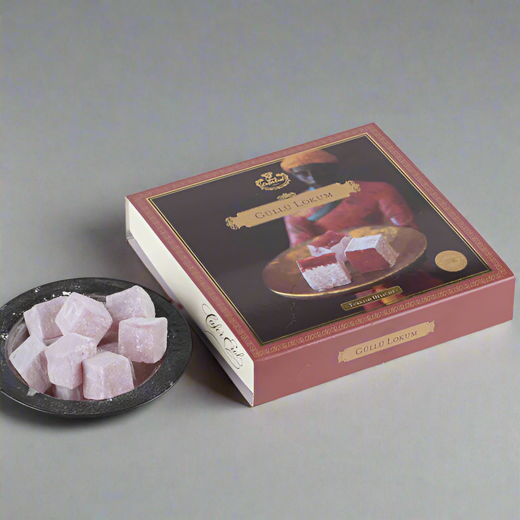 An envelope cardboard box with a floral design, containing rose Turkish delight, displayed on a marble surface with a bowl of the same Turkish delight in front.