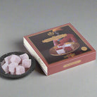 An envelope cardboard box with a floral design, containing rose Turkish delight, displayed on a marble surface with a bowl of the same Turkish delight in front.