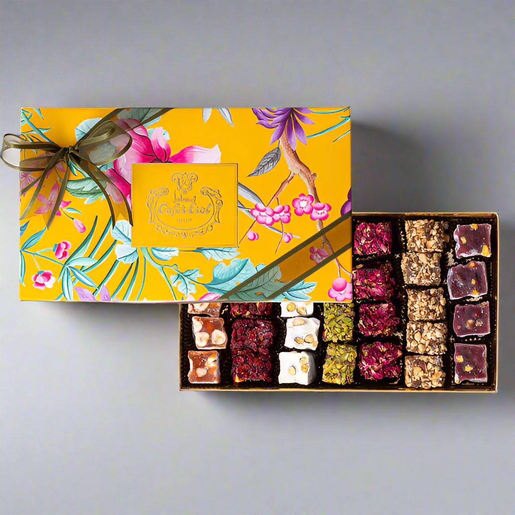 A decorative cardboard box of Mixed Roll Turkish Delights, with a floral pattern on the cover, and a variety of rolled sweets with different fillings visible through the transparent lid.